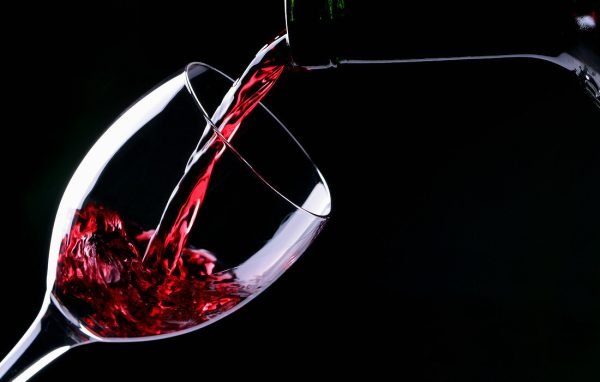 Ein Glas Rotwein eingiessen, schwarzer Hintergrund